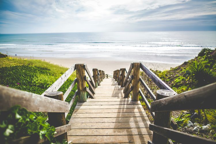 A brown wooden walkway near beach during daytime